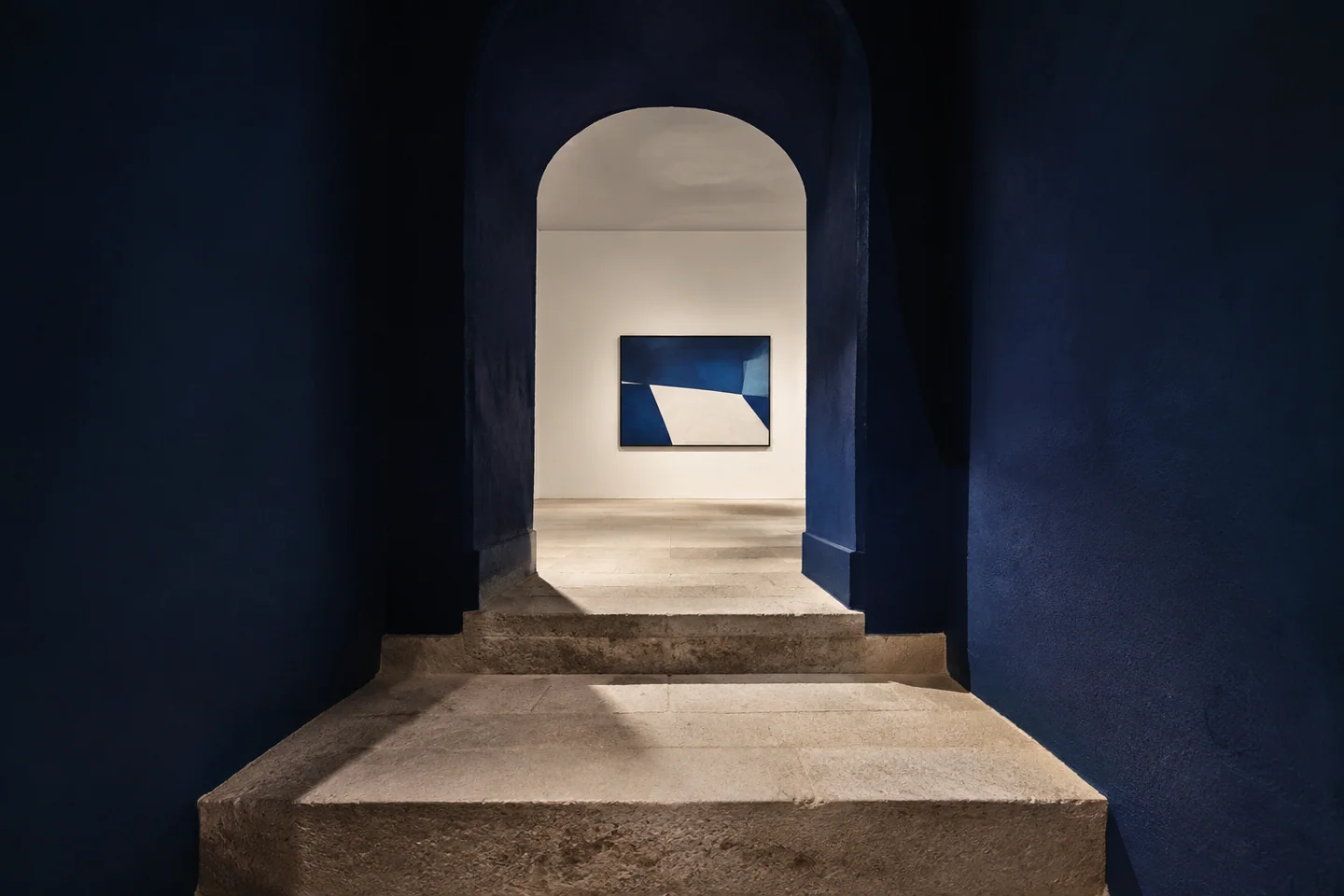 Composition d’intention : trois marches de pierre mènent à travers une arche bleu nuit vers une œuvre éclairée.